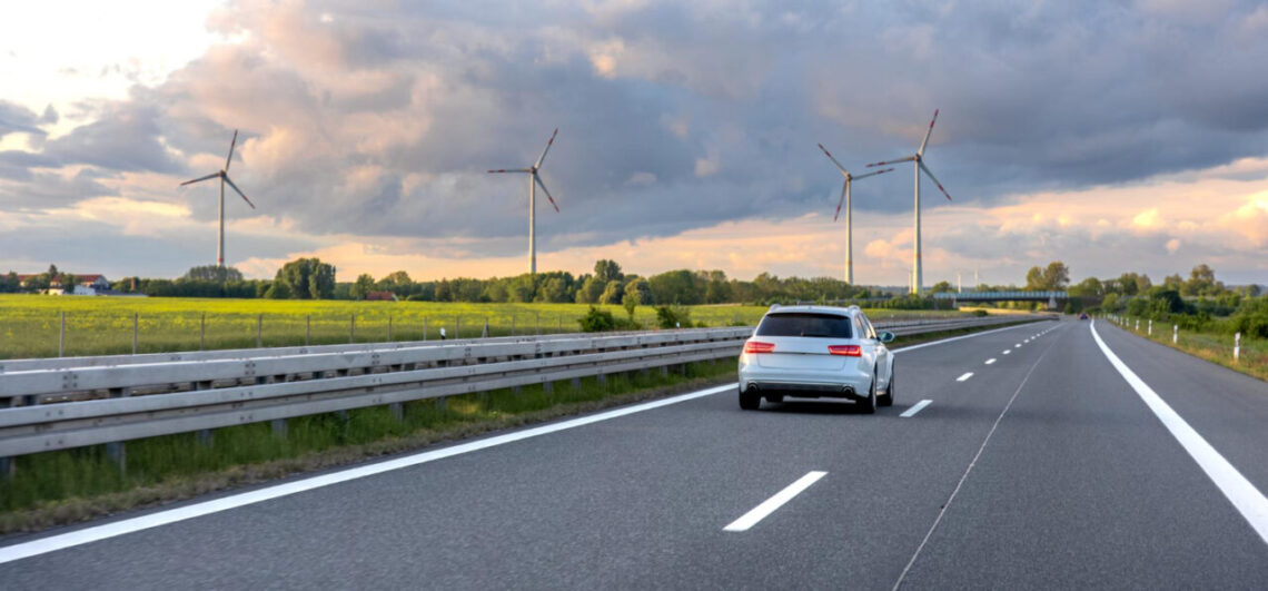 Illustration d’une voiture de société roulant sur autoroute avec éoliennes, symbolisant la réforme 2025 et la mobilité durable en entreprise.
