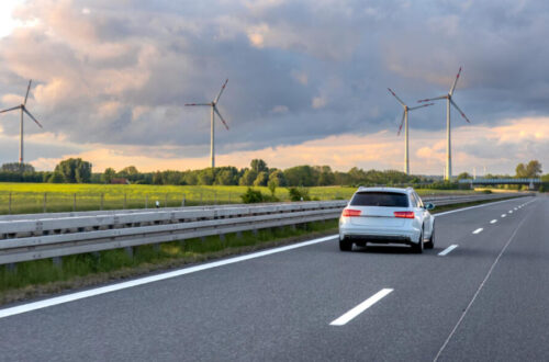 Illustration d’une voiture de société roulant sur autoroute avec éoliennes, symbolisant la réforme 2025 et la mobilité durable en entreprise.