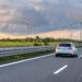 Illustration d’une voiture de société roulant sur autoroute avec éoliennes, symbolisant la réforme 2025 et la mobilité durable en entreprise.