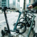 Un usager urbain compare plusieurs mobilités électriques légères le long d’une rue moderne, en observant attentivement scooters et vélos électriques.