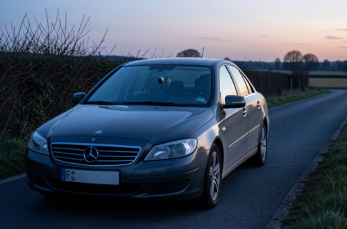 Voiture banalisée sombre circulant au crépuscule sur une route départementale française, avec une caméra radar discrète derrière le pare-brise.