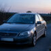 Voiture banalisée sombre circulant au crépuscule sur une route départementale française, avec une caméra radar discrète derrière le pare-brise.